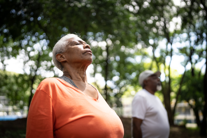 A senior woman practicing breathing exercises outdoors.