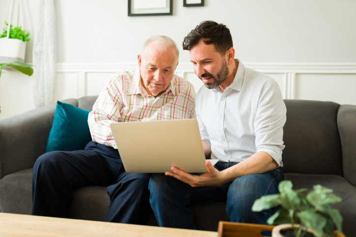 Senior man and younger man sitting on a couch looking at a laptop together