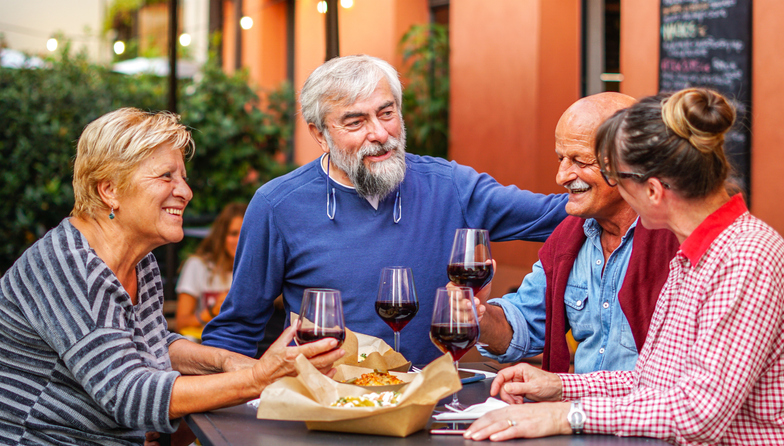 Happy older adult friends drinking wine during dinner.