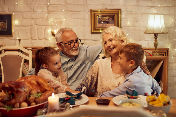 Happy grandparents talking to their grandchildren at the dining table at home.