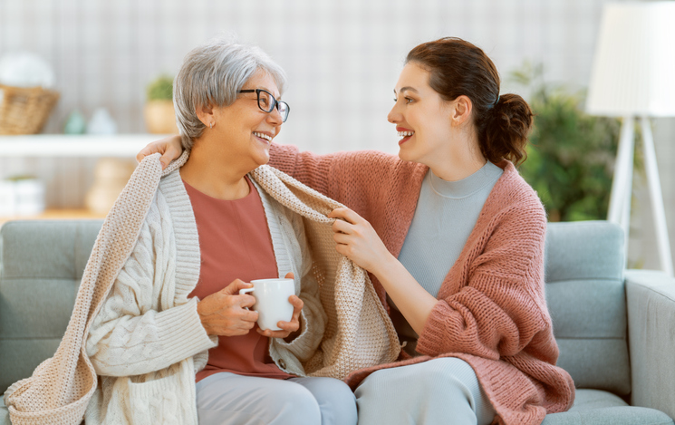 Beautiful mother and daughter are talking and smiling while sitting on the couch at home.