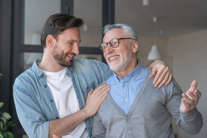 Adult man and senior father smiling and hugging outdoors.