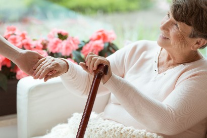 elderly woman holding someones hand as she sits in a chair with her cane in hand